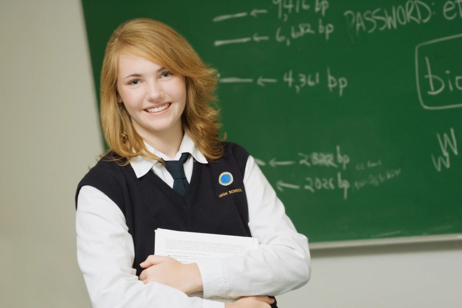 A girl in front of a chalkboard holding papers.