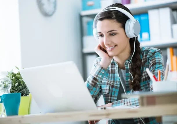 A woman wearing headphones looking at her laptop.